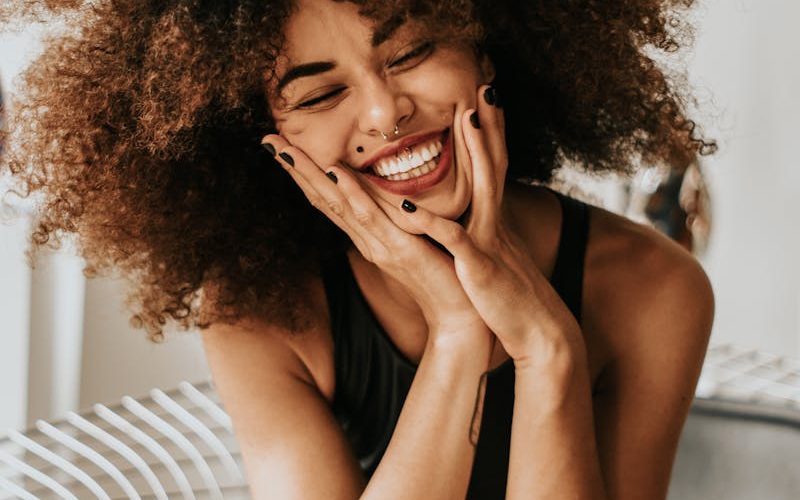 A cheerful woman with an afro hairstyle sitting indoors, showcasing happiness and style.